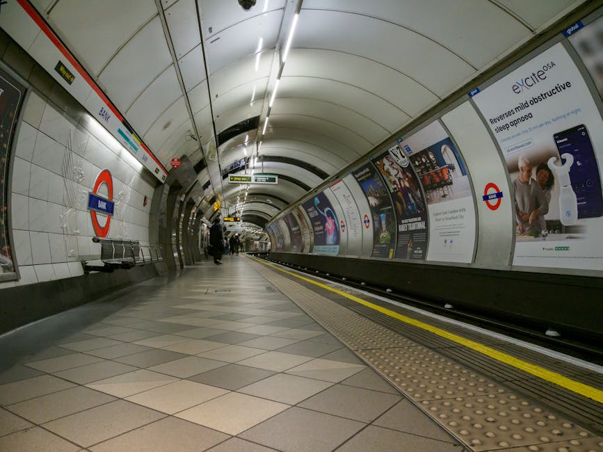 A set of concrete stairs leading up to a higher level within a busy underground train station, with several commuters ascending and descending. The staircase is flanked by stainless steel handrails an